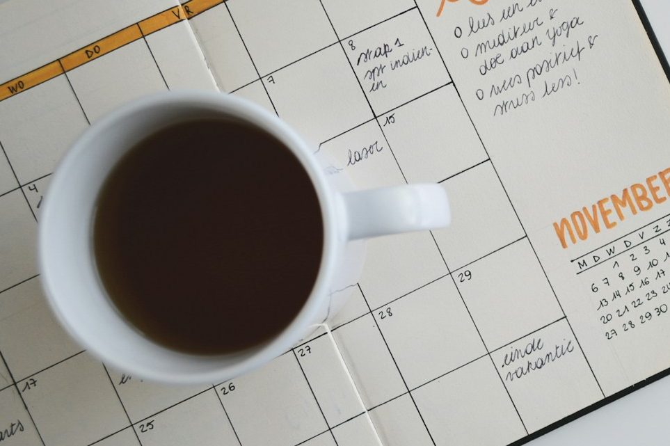 Termine.jpg Tasse mit schwarzem Kaffee auf einem Wandkalender.