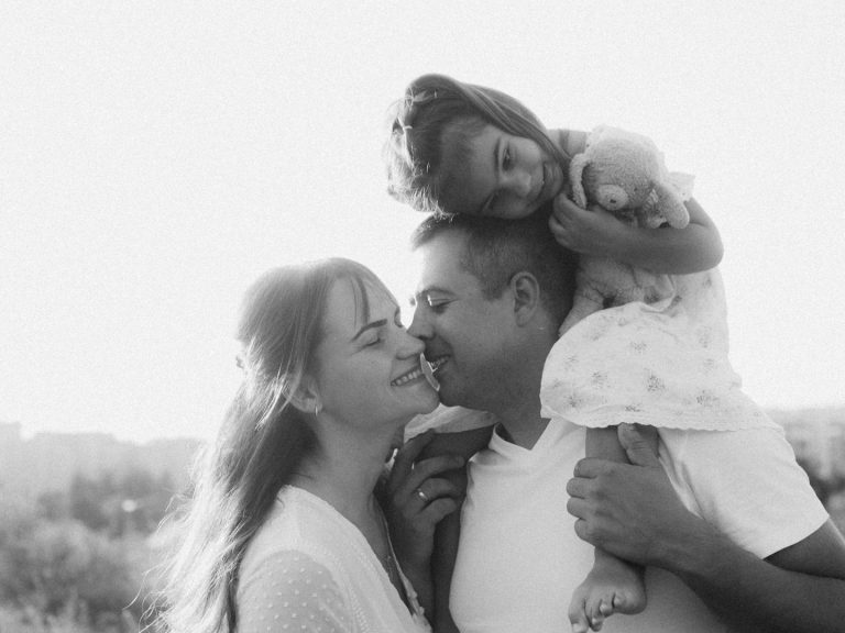 Familie.jpg Lächelndes Paar mit Kind auf den Schultern in einer sonnigen Landschaft.