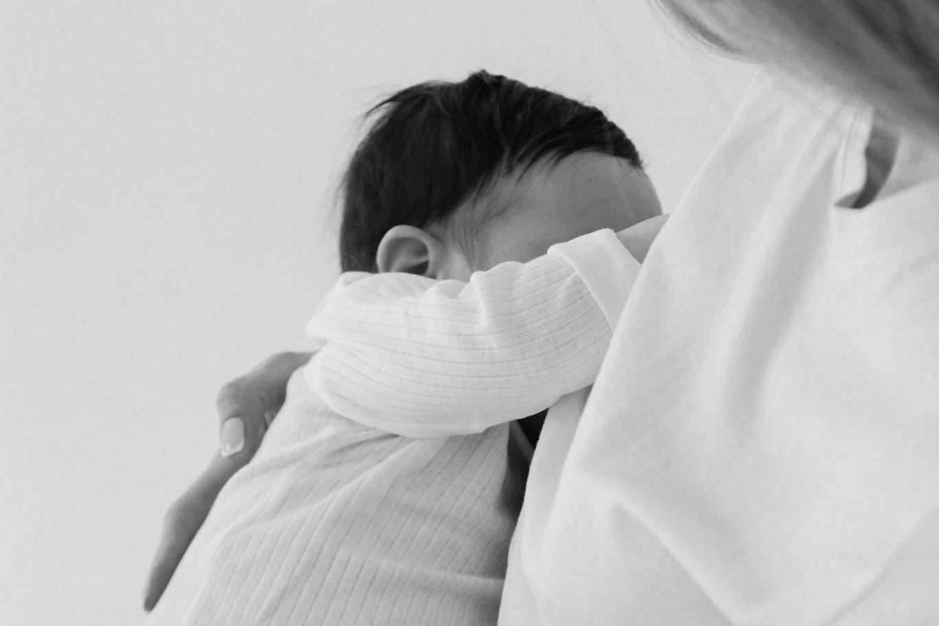 Stillberatung.jpg Ein Baby, das sich in den Armen einer Erwachsenen an die Schulter schmiegt.